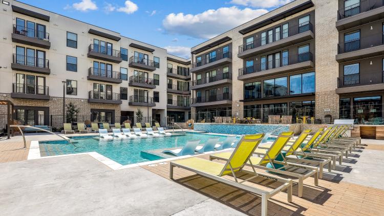 Pool with deck chairs and an apartment building behind it